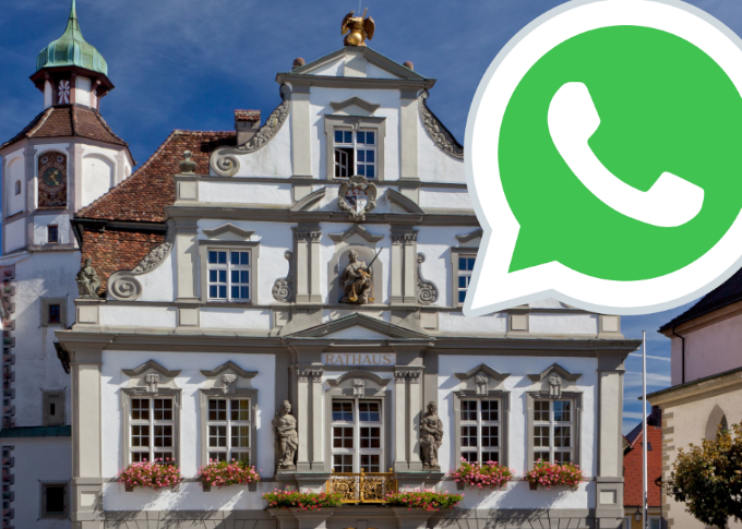 Ein historisches Gebäude mit aufwendiger Architektur, das als Rathaus dient. Vor der Fassade sind Blumenkästen sichtbar. In der oberen rechten Ecke ist das Logo von WhatsApp in grünem Hintergrund abgebildet.