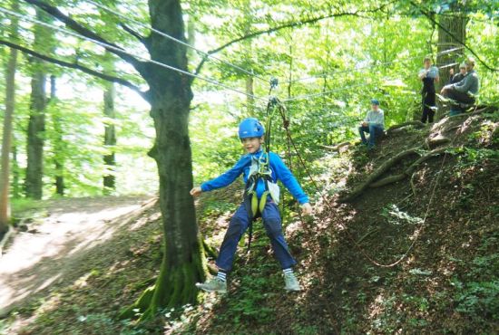 Ein Kind schwebt im Wald an einer Seilbahn