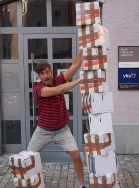 Schauspieler Florian Thunemann hält einen Stapel Kartons fest. 