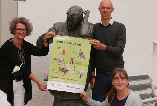Zwei Frauen und ein Mann halten ein Plakat