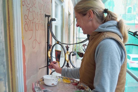 Frau mit Farbpalette und Pinsel auf einem Gerüst