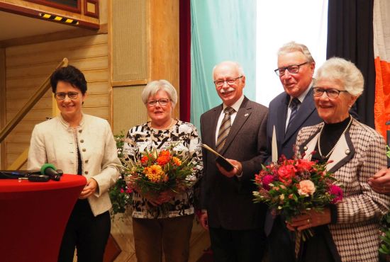 Ministerin und zwei Frauen mit Blumen und zwei Männer