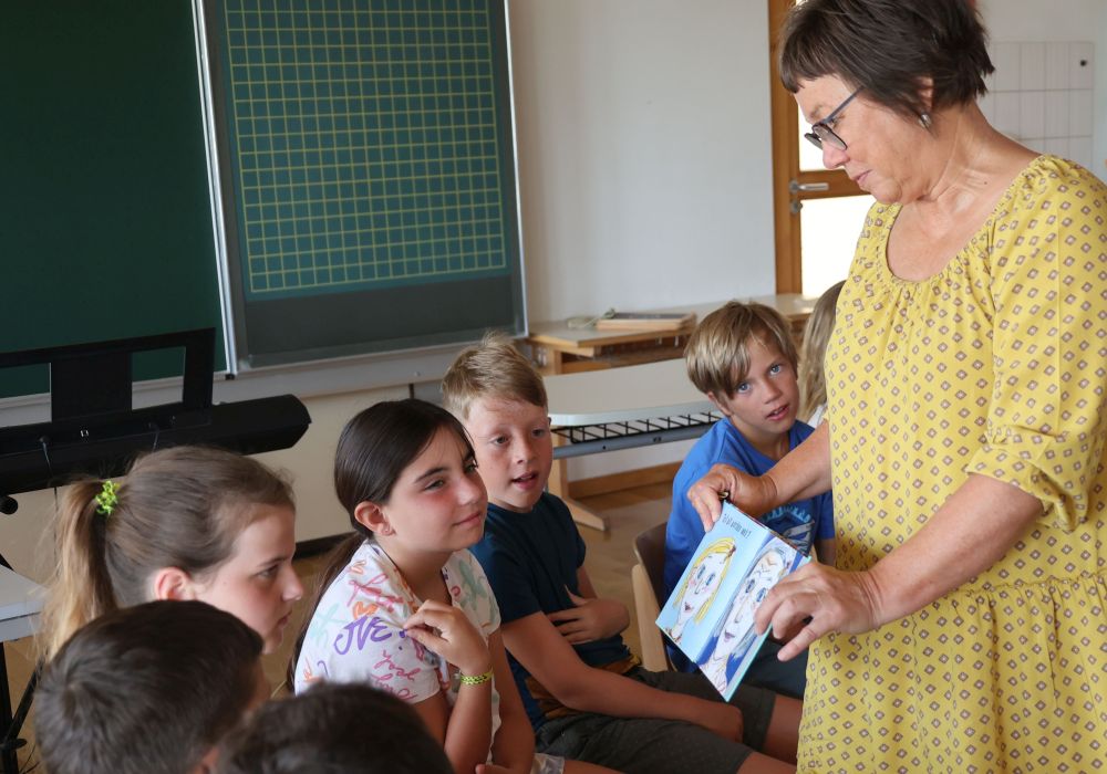 Frau zeigt Kindern ein Buch mit den Bildern einer alten Frau und sie als Kind