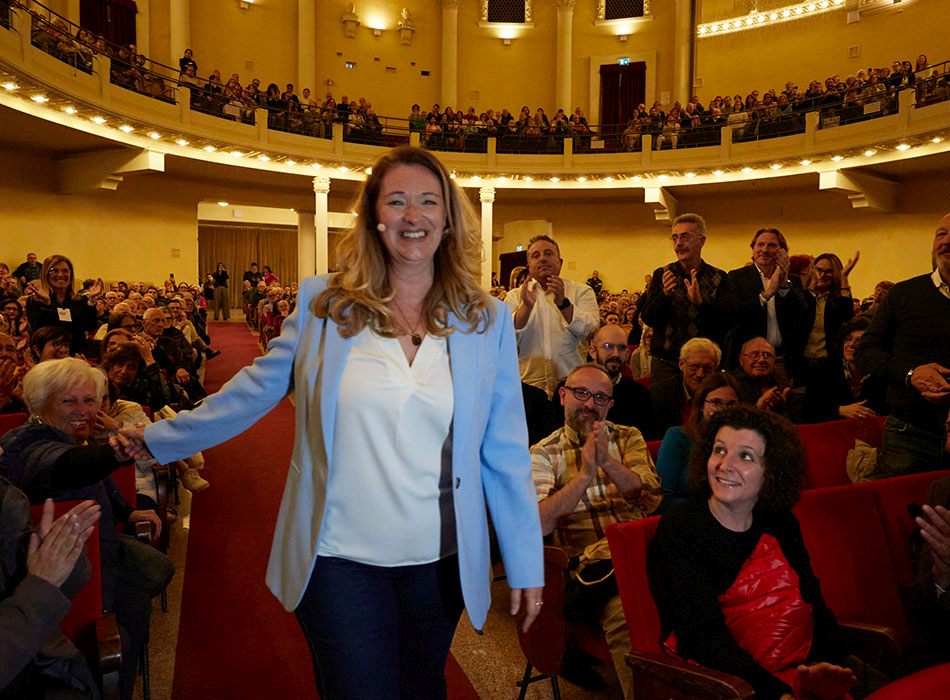 Eine Frau in einem großen Raum, viele Menschen applaudieren