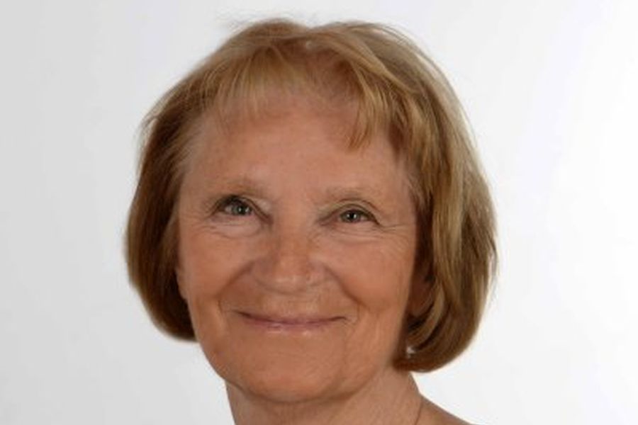 Ein lächelnde ältere Frau mit kurzen, hellbraunen Haaren und einem freundlichen Gesichtsausdruck auf einem neutralen Hintergrund.