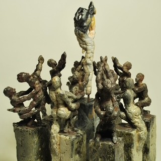 Die Skulptur zeigt eine Gruppe von menschlichen Figuren, die um eine zentrale Figur angeordnet sind. Die zentrale Figur hebt sich ab und scheint eine besondere Bedeutung zu haben, während die anderen Figuren unterschiedliche Posen einnehmen, die Bewegung und Interaktion ausdrücken.