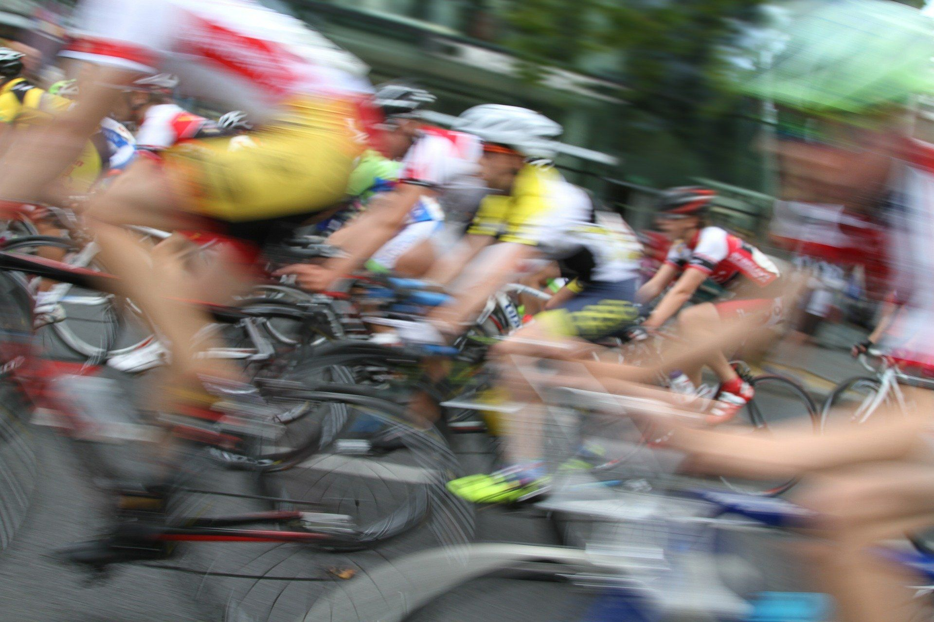Eine Gruppe von Radfahrern in schneller Bewegung während eines Rennens, unscharf dargestellt, um die Dynamik der Szene zu betonen. Die Sportler tragen verschiedene Trikots und Helme.