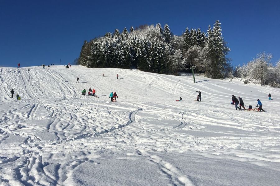 Viele Menschen fahren Ski und rodeln den Berg an der Berger Höhe hinunter