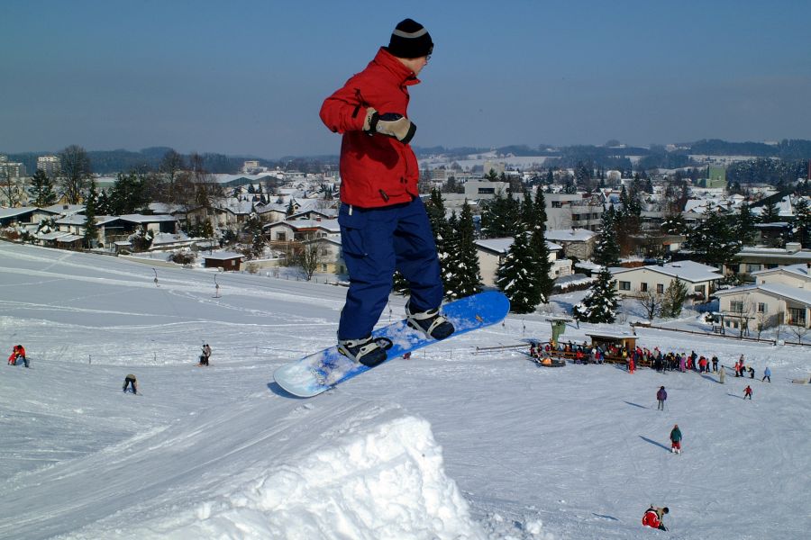 Jugendlicher springt mit einem Snowboard über eine Schanze aus Schnee Bild