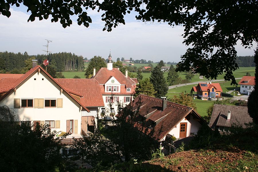 Blick auf das Rathaus in Leupolz zwischen Bäumen, Sträucher und Häusern hindurch Bild