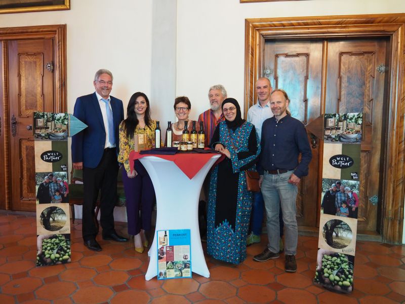 Sieben Männer und Frauen stehen hinter einem Stehtisch und präsentieren stolz Fair-Trade-Produkte Bild