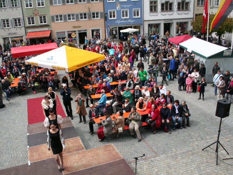 Blick aus dem Rathaus auf den Marktplatz, Modenschau mit vier Models auf der Bühne, zahlreiche Zuschauerinnen und Zuschauer an Biertischen und -bänken