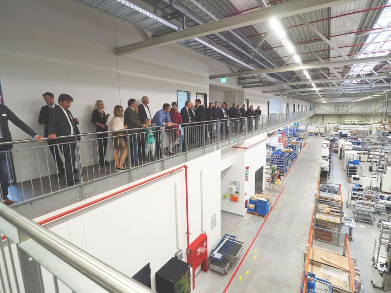 Eine Gruppe von Menschen stehen in einer großen Halle auf einer Galerie und blicken in die Produktionshalle