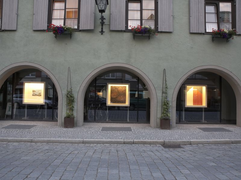 Drei Gemälde in beleuchteten Vitrinen in drei Schaufenstern unter Torbögen Bild