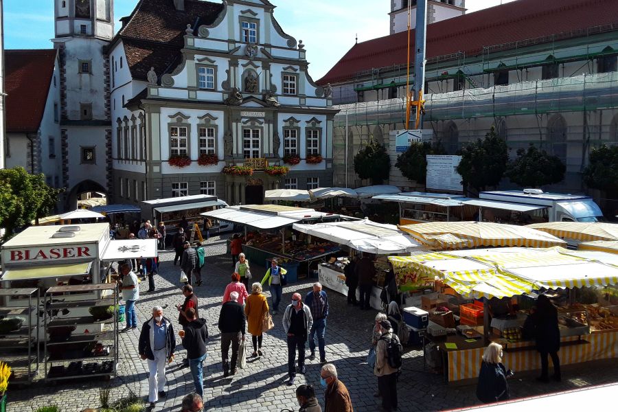 Wochenmarkt mit Marktständen und Besuchern im Vordergrund sowie dem Wangener Rathaus im Hintergrund Bild