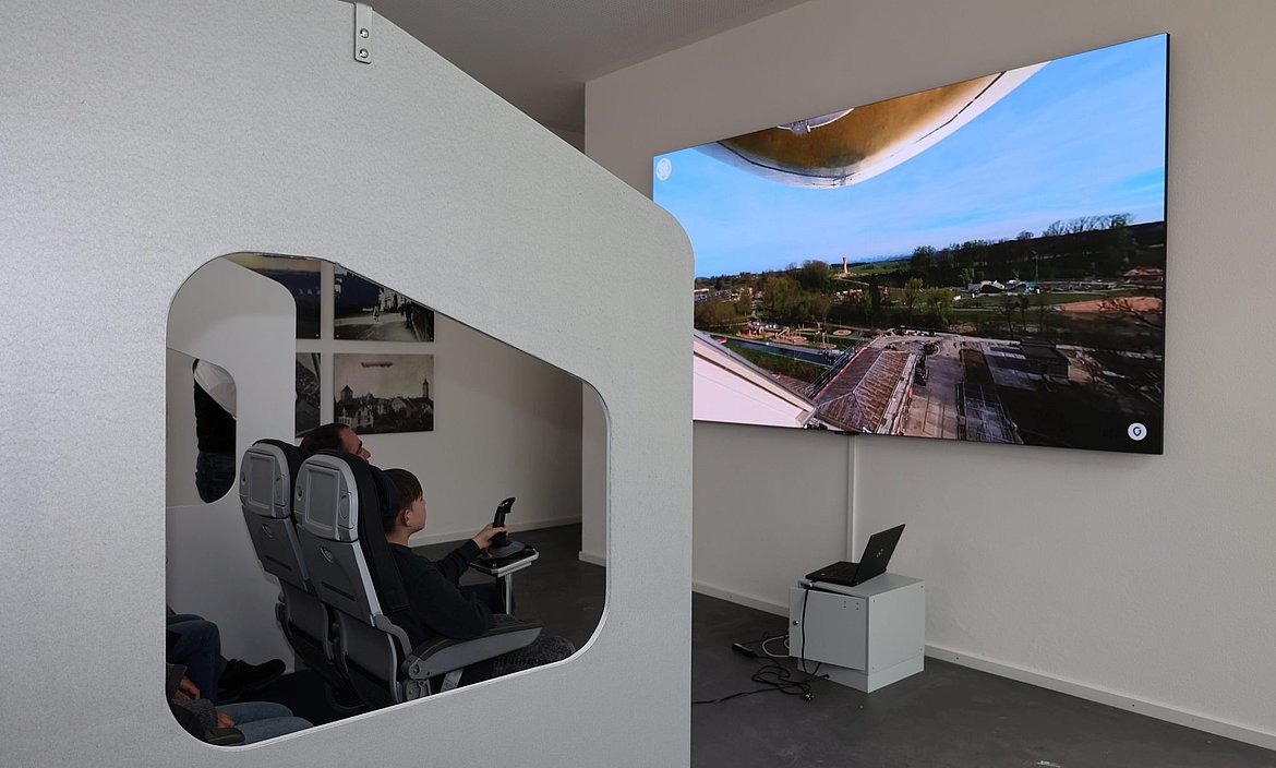 Blick auf einen großen Monitor mit der Parklandschaft davor sitzen 2 Personen