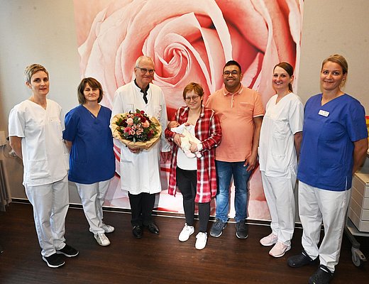 Eltern von Emma mit dem Baby, Chefarzt und vier weiteren Klinikmitarbeitenden