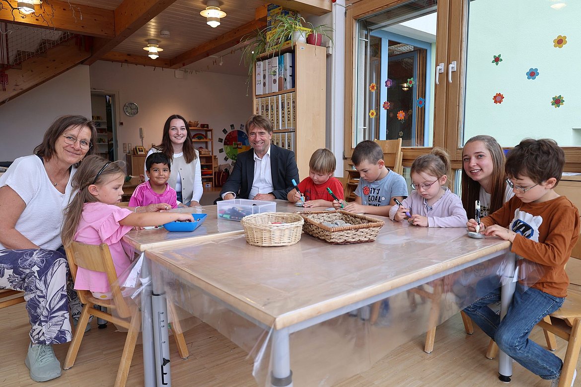 Kinder spielen und werkeln mit ihren Erzieherinnen und Oberbürgermeister Michael Lang an einem Tisch.