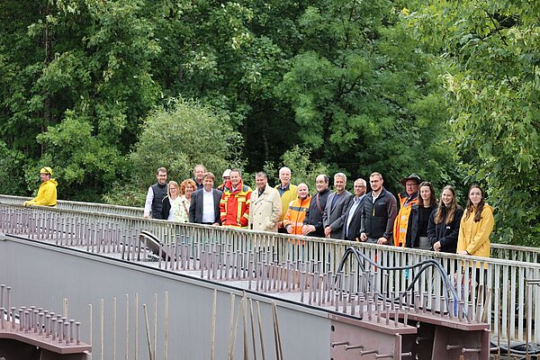 Männer und Frauen neben der im Bau befindlichen Brücke