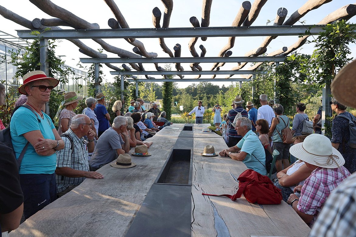 Viele Menschen an einem langen Tisch im ERBA-PArk. OB Lang spricht.