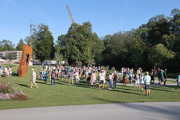 Park in den Auwiesen mit vielen Menschen und dem Kunstwerk aus Cortenstahl