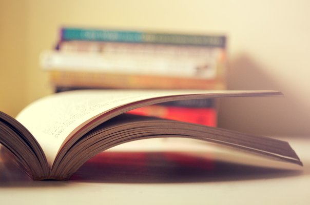 Ein aufgeschlagenes Buch im Vordergrund, ein Bücherstapel im Hintergrund