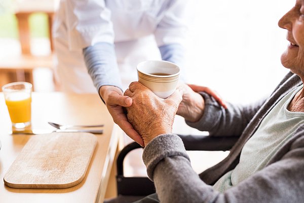 Pflegende reicht einer Person eine Tasse