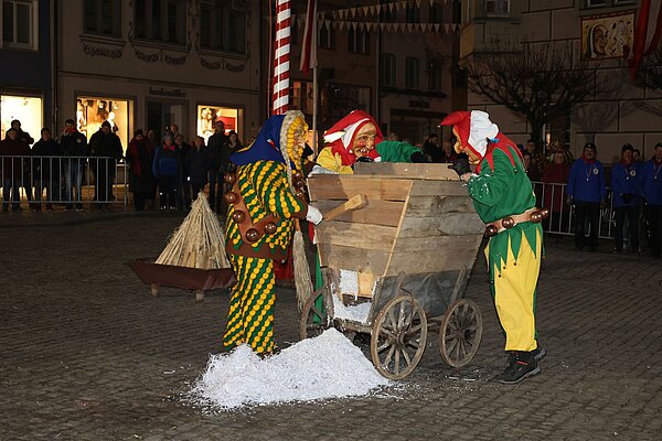 Narren lassen aus einem holzwagen geschreddertes Papier fallen