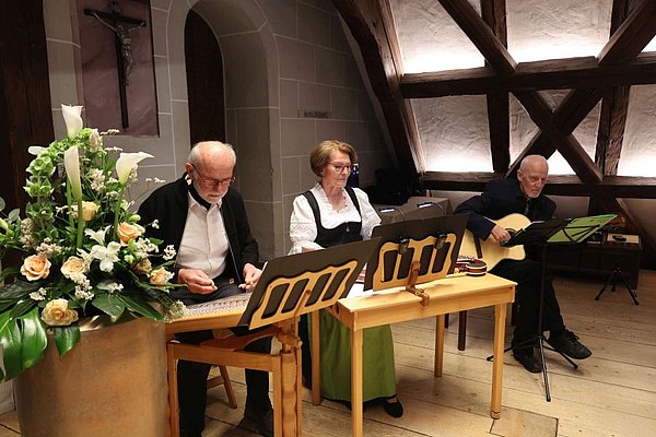 Stubenmusik Appelt, 2 Männer und eine Frau sitzen an ihren Instrumenten (Hackbrett, Zitter und Gitarre) und umrahmen die Feier musikalisch.