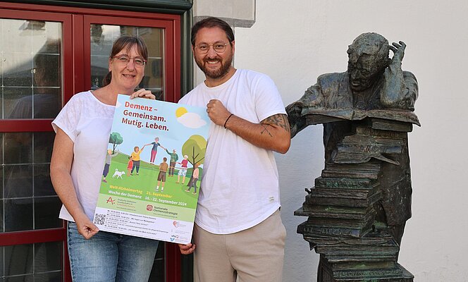 Eine Frau und ein Mann halten ein Plakat. Es wirbt für die Woche der Demenz