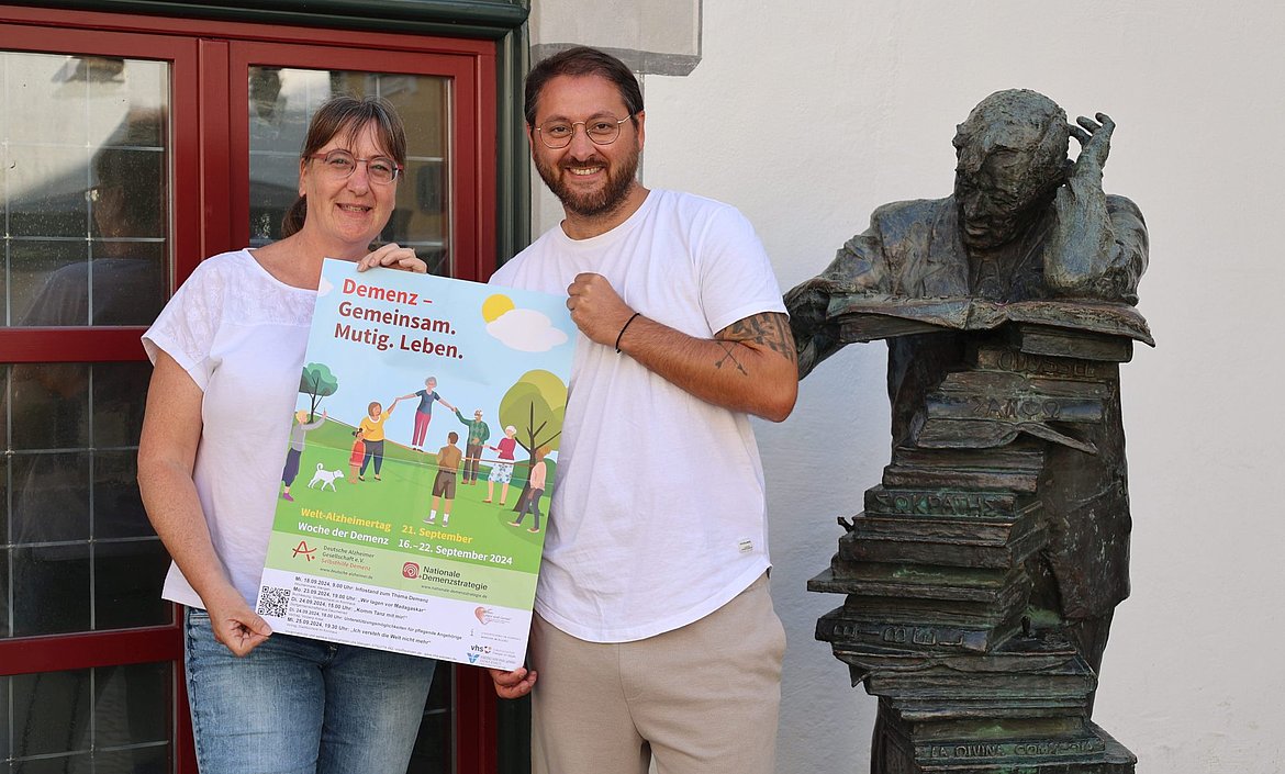 Eine Frau und ein Mann halten ein Plakat. Es wirbt für die Woche der Demenz