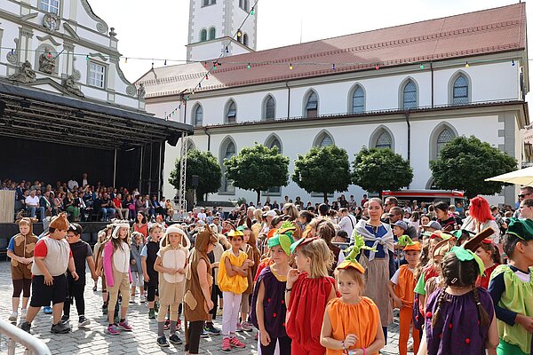 Viele Kinder in bunten Kostümen mit Obst aus Stoff auf dem Kopf