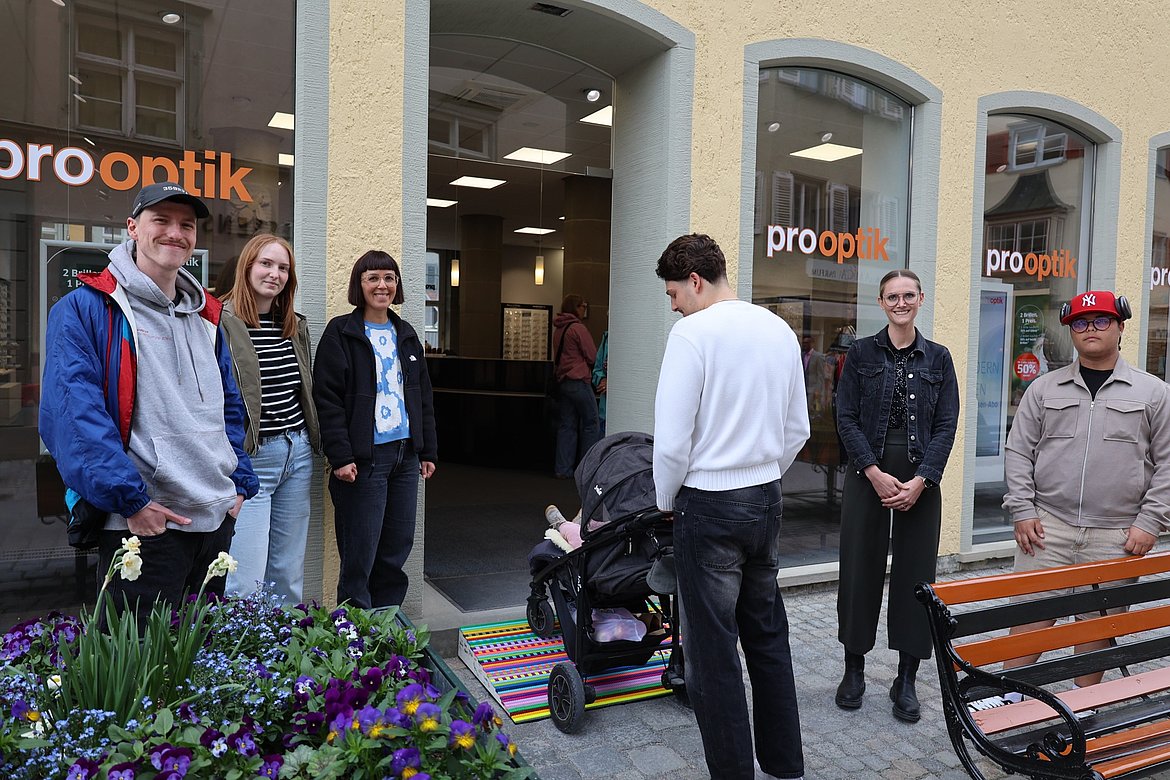 Mehrere Personen beobachten einen jungen Mann. Er schiebt einen Kinderwagen über eine Rampe.
