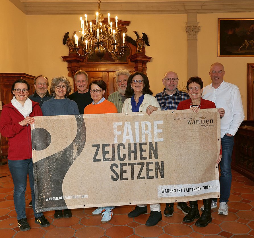 Zehn Personen stehen nebeneinander. Sie halten ein Banner mit dem Schriftzug: Faire Zeichen setzen