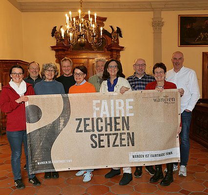 Zehn Personen stehen nebeneinander. Sie halten ein Banner mit dem Schriftzug: Faire Zeichen setzen
