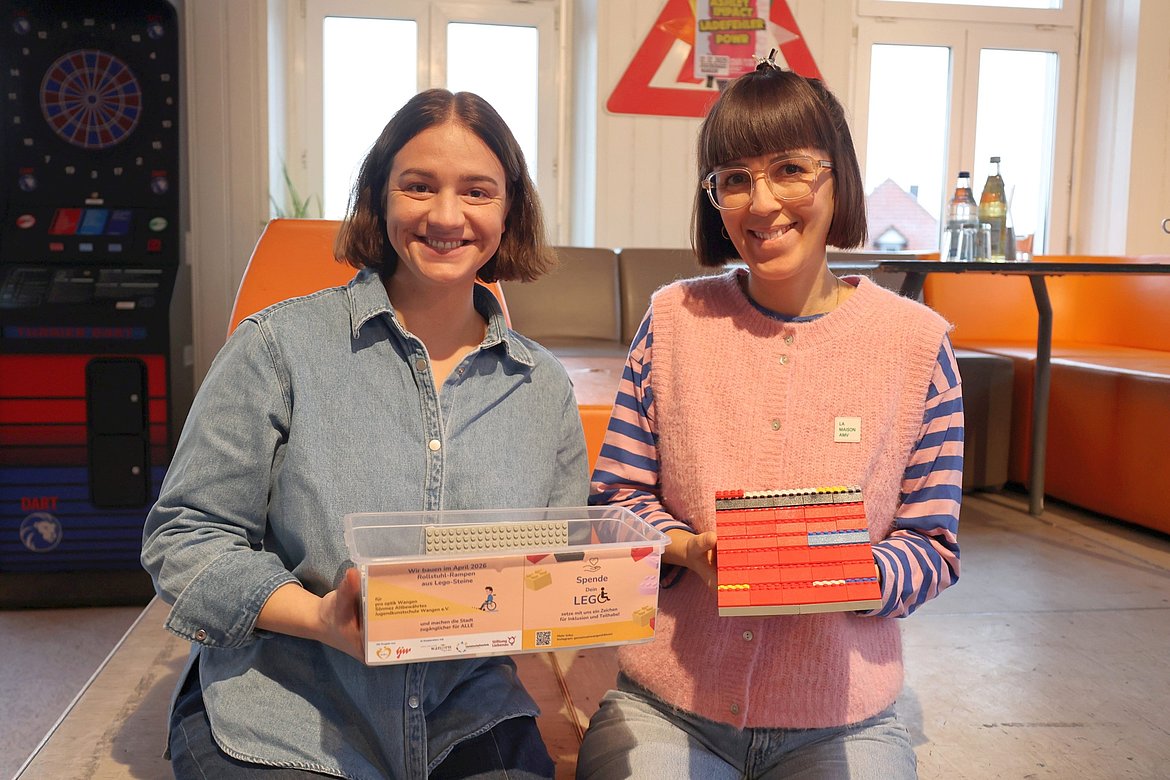 Zwei Frauen. Sie halten eine leere Box und eine symbolisch gebaute kleine Rampe in der Hand.