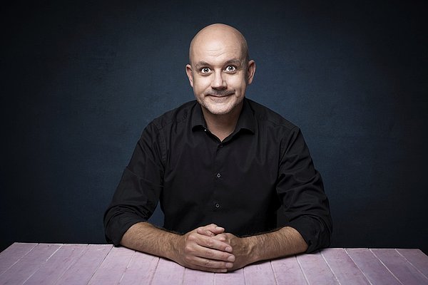 Ein Mann sitzt an einem Tisch und schaut den Betrachter an