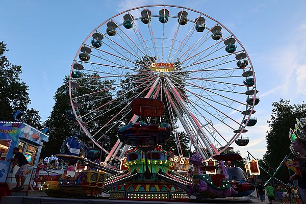 Riesenrad mit bunten Lichtern, davor das Kinderkarussell