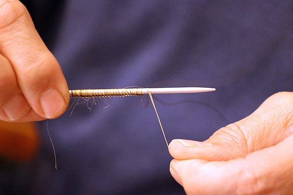 Eine Stricknadel mit Schlingen aus Haaren und unten einem Metalldraht