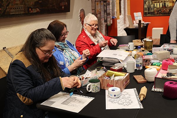 Drei Frauen im Museum zeigen eine besondere Handarbeitstechnik.