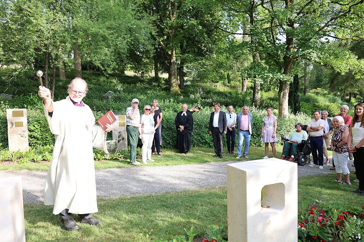 Pastoralreferent schwingt den Weihwasserwedel. Menschen schauen zu