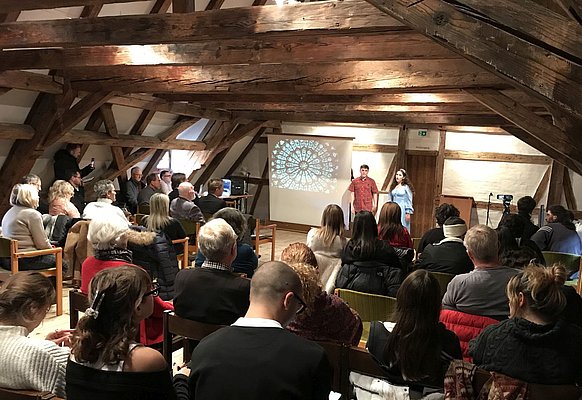 Ein junger Mann und eine junge Frau tragen vor einem Publikum etwas vor.