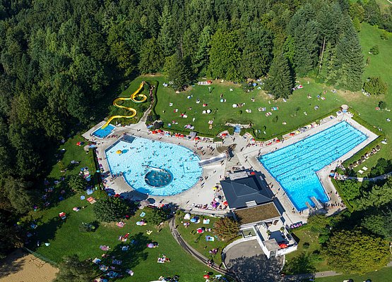 Blick von oben auf das Freibad Stefanshöhe mit zwei großen Becken, Rutsche und Kinderbecken