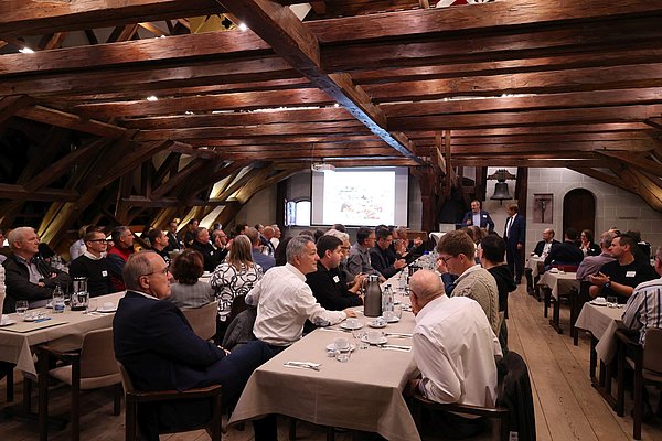Viele Personen sitzen an langen Tischen und hören zu