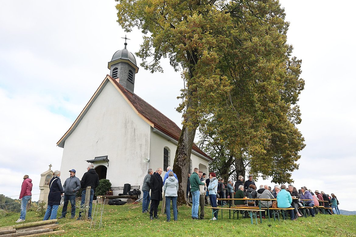 Kapelle Niederwangen und Menschen auf Bierbänken davor.