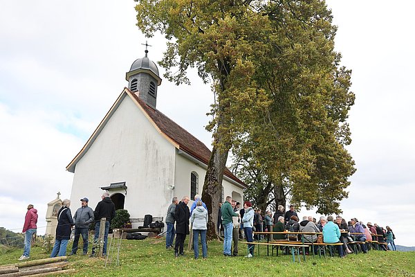 Kapelle Niederwangen und Menschen auf Bierbänken davor.