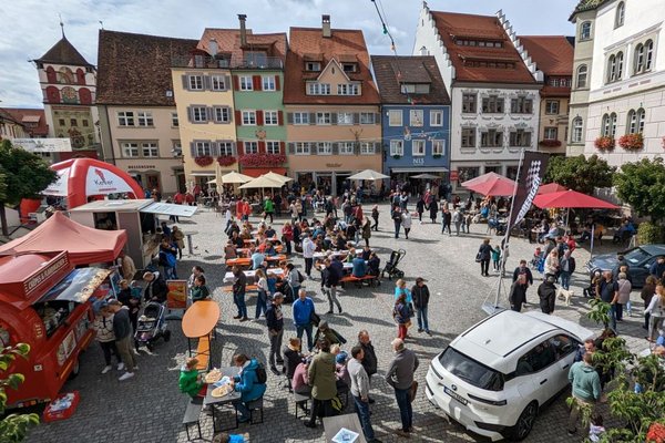 Blick auf den Marktplatz, es sind ausgestellte Autos, viele Menschen und Verkaufsstände zu sehen.