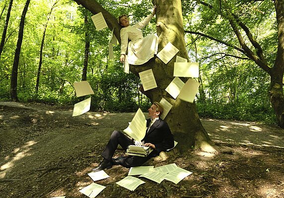 Zwei Menschen sitzen im Wald und werfen beschriebenes Papier in die Luft