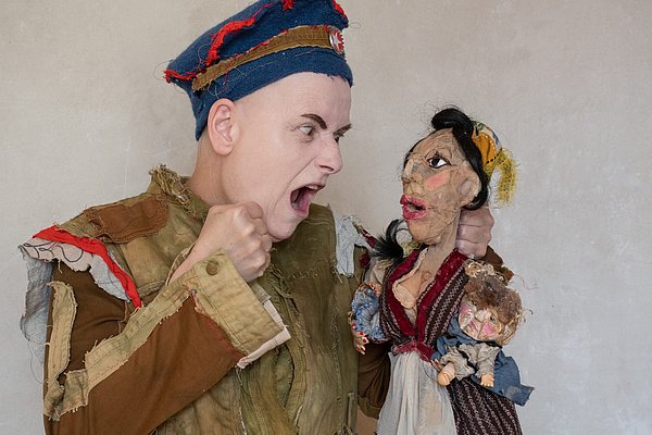 Ein Mensch mit einer Art Kasper-Figur. Beide sind verkleidet.