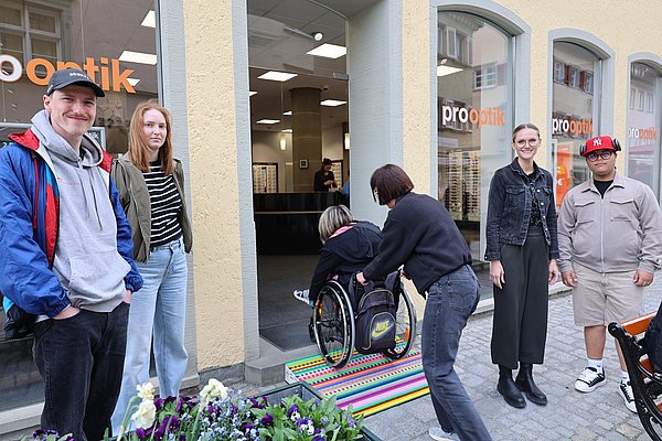 Eine Frau schiebt eine Rollstuhlfahrerin über die neue Rampe. Das Team schaut zu.